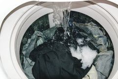Lavatrice a carica dall'alto piena di vestiti bagnati e acqua saponata che si riversa dentro