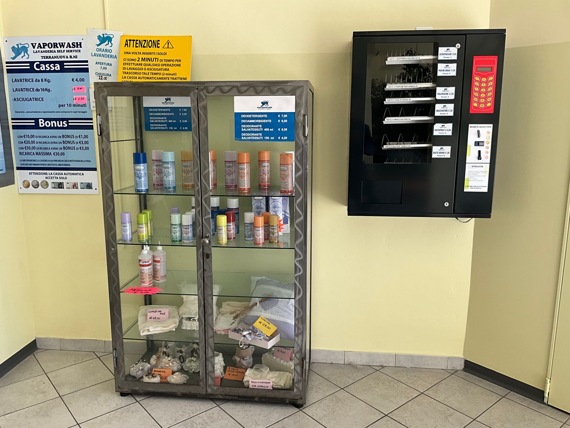 Parete della hall con una vetrina per snack e un distributore automatico nero accanto ad avvisi affissi.