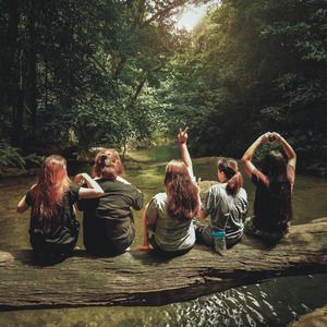 A group of people are sitting on a log over a river.