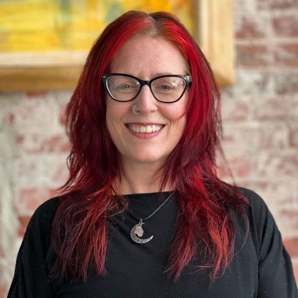 a woman with red hair is wearing glasses and a necklace with a crescent moon pendant