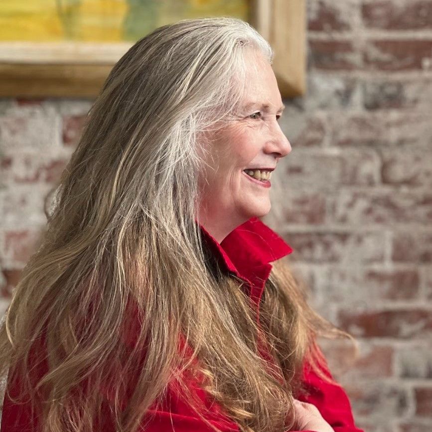 a woman with long gray hair is smiling in front of a brick wall