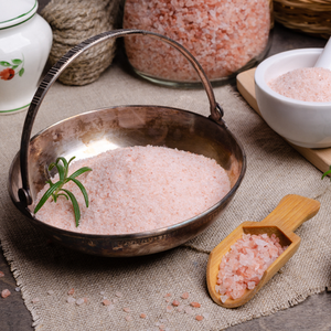a bowl of pink salt next to a wooden scoop