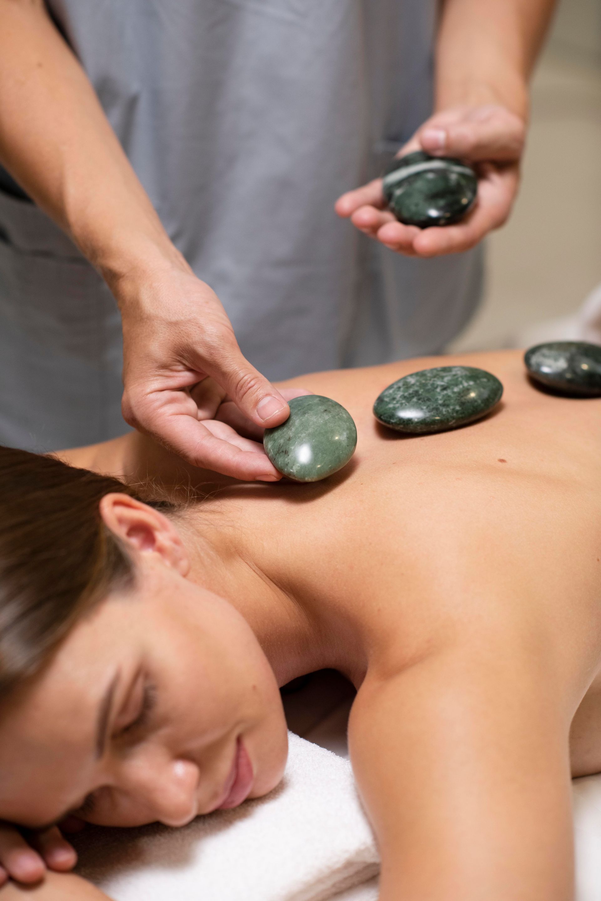 a woman is getting a massage with green rocks on her back