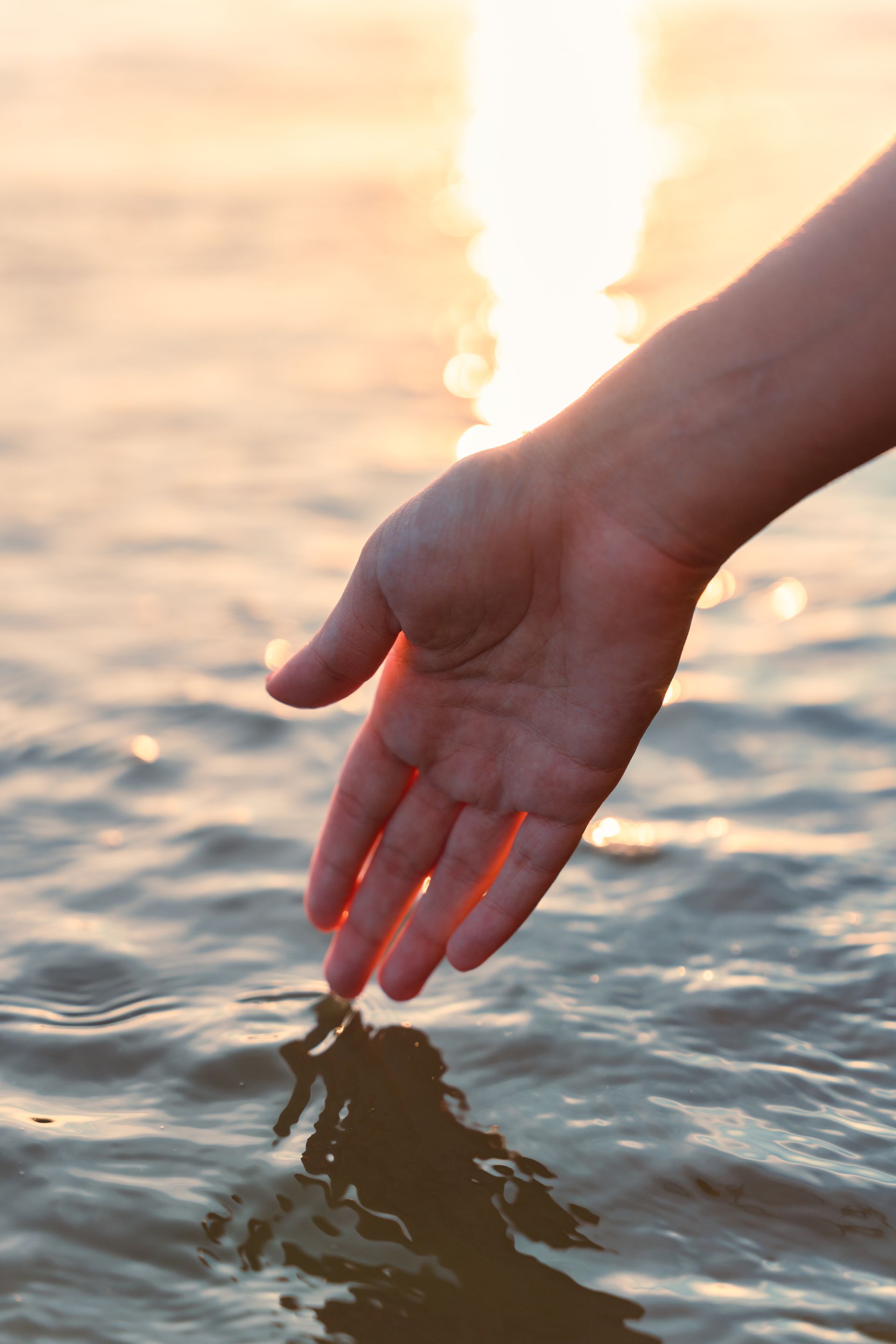 a woman 's hand is touching the water in the ocean .