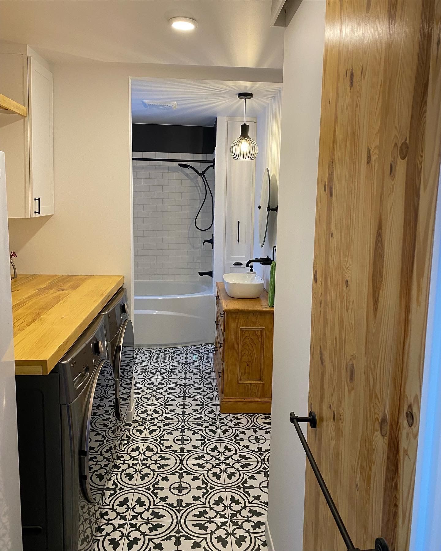 Buanderie et salle de bains étroites avec carrelage à motifs, lave-linge/sèche-linge, murs blancs et éléments en bois.