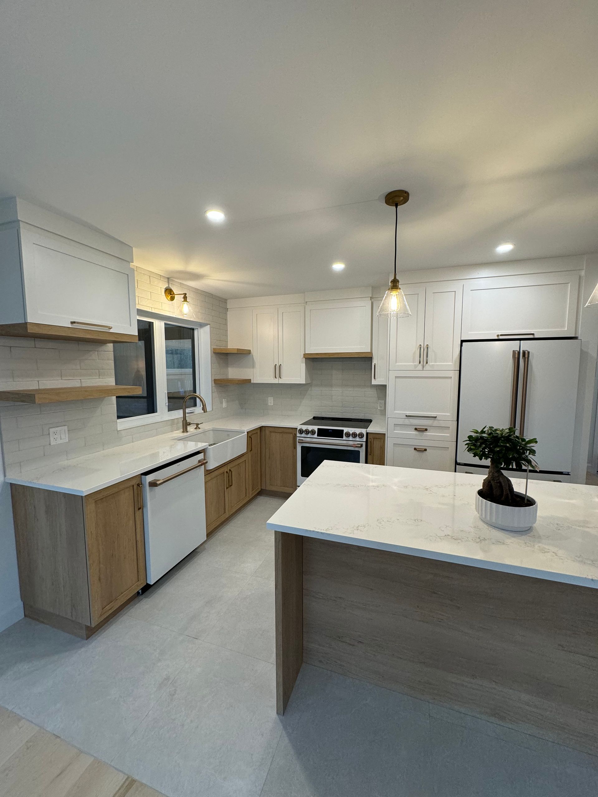 Cuisine moderne avec placards blancs et en bois clair, plans de travail clairs et îlot central.