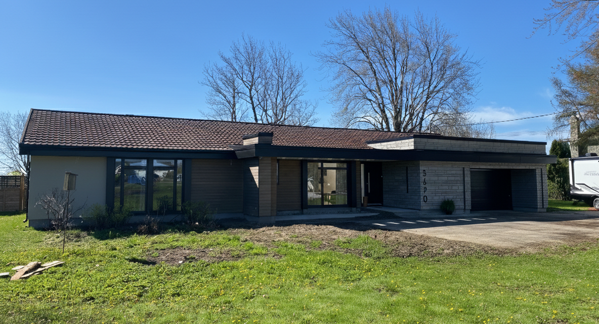 Une maison de plain-pied, discrète, avec un toit plat, de grandes fenêtres et une porte de garage, située dans un jardin gazonné sous un ciel bleu.