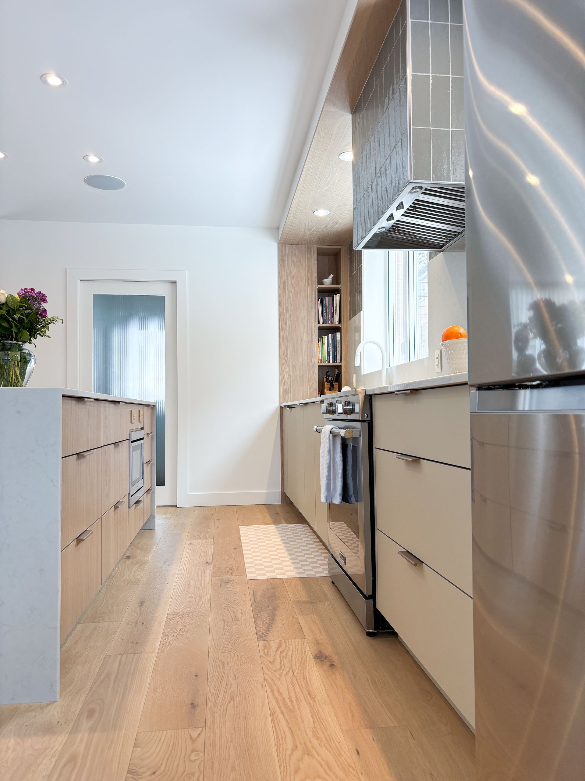 Cuisine moderne avec planchers de bois clair, armoires claires, électroménagers en acier inoxydable et îlot central.