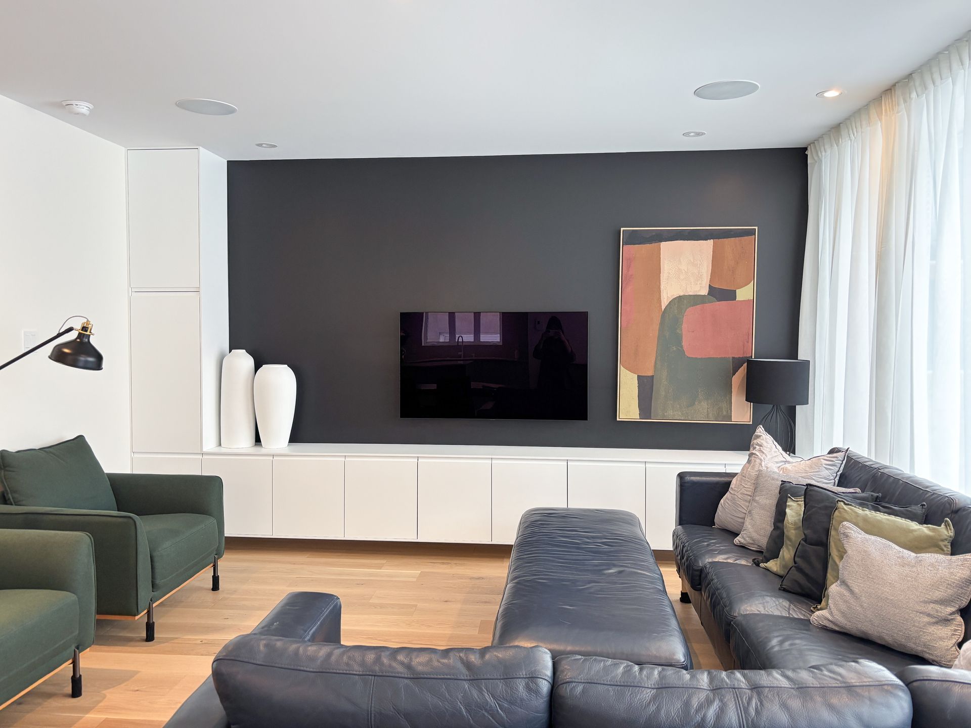 Salon moderne avec mur d'accent gris foncé, télévision montée, rangement blanc et canapé sectionnel bleu foncé.