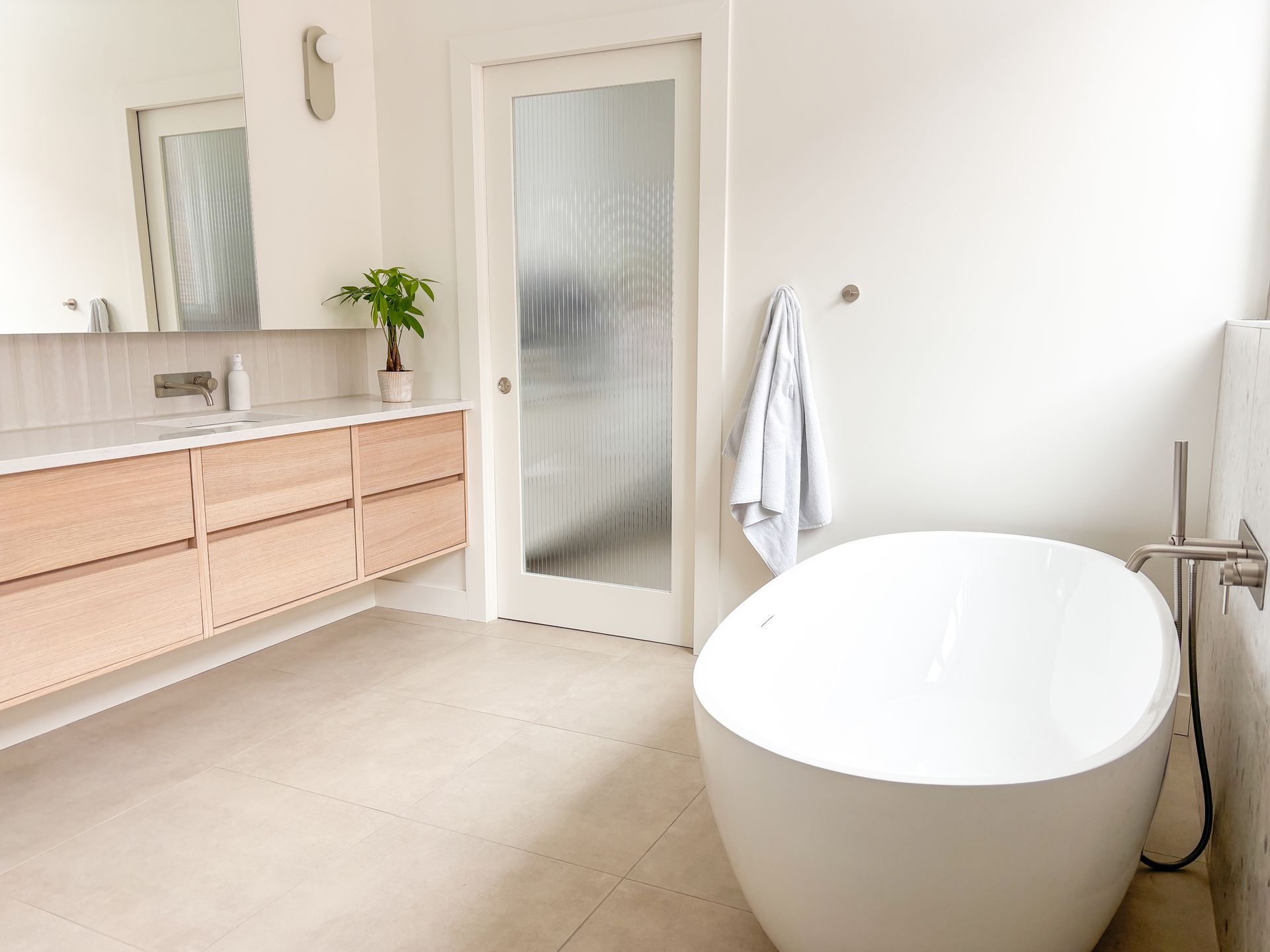 Salle de bain blanche moderne avec baignoire autoportante, vanité en bois et porte en verre dépoli.