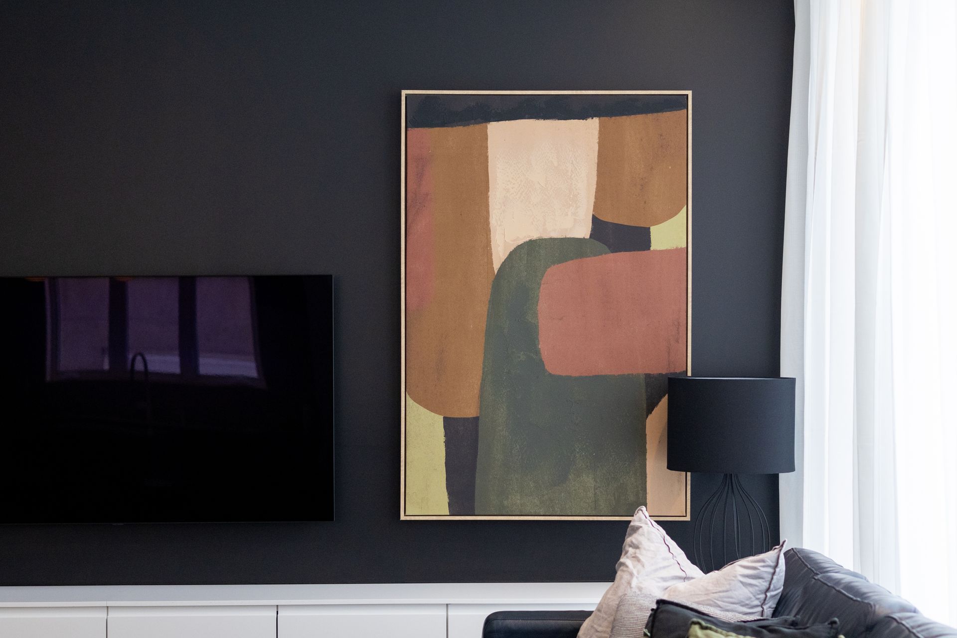 Salon moderne avec œuvre d'art abstraite, télévision montée et lampe noire.