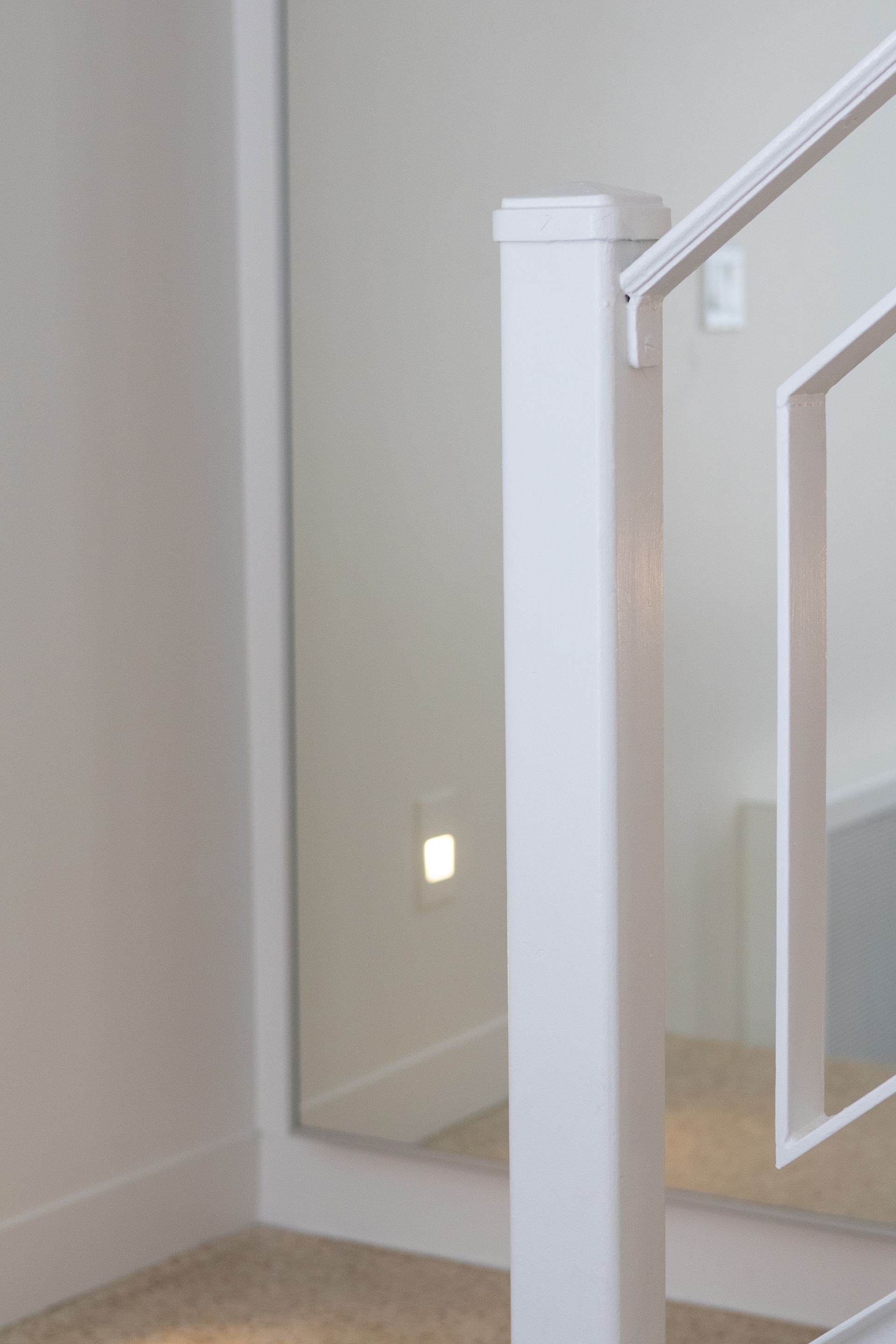 Poteau de rampe d'escalier blanc à côté d'un mur avec un éclairage encastré intégré.