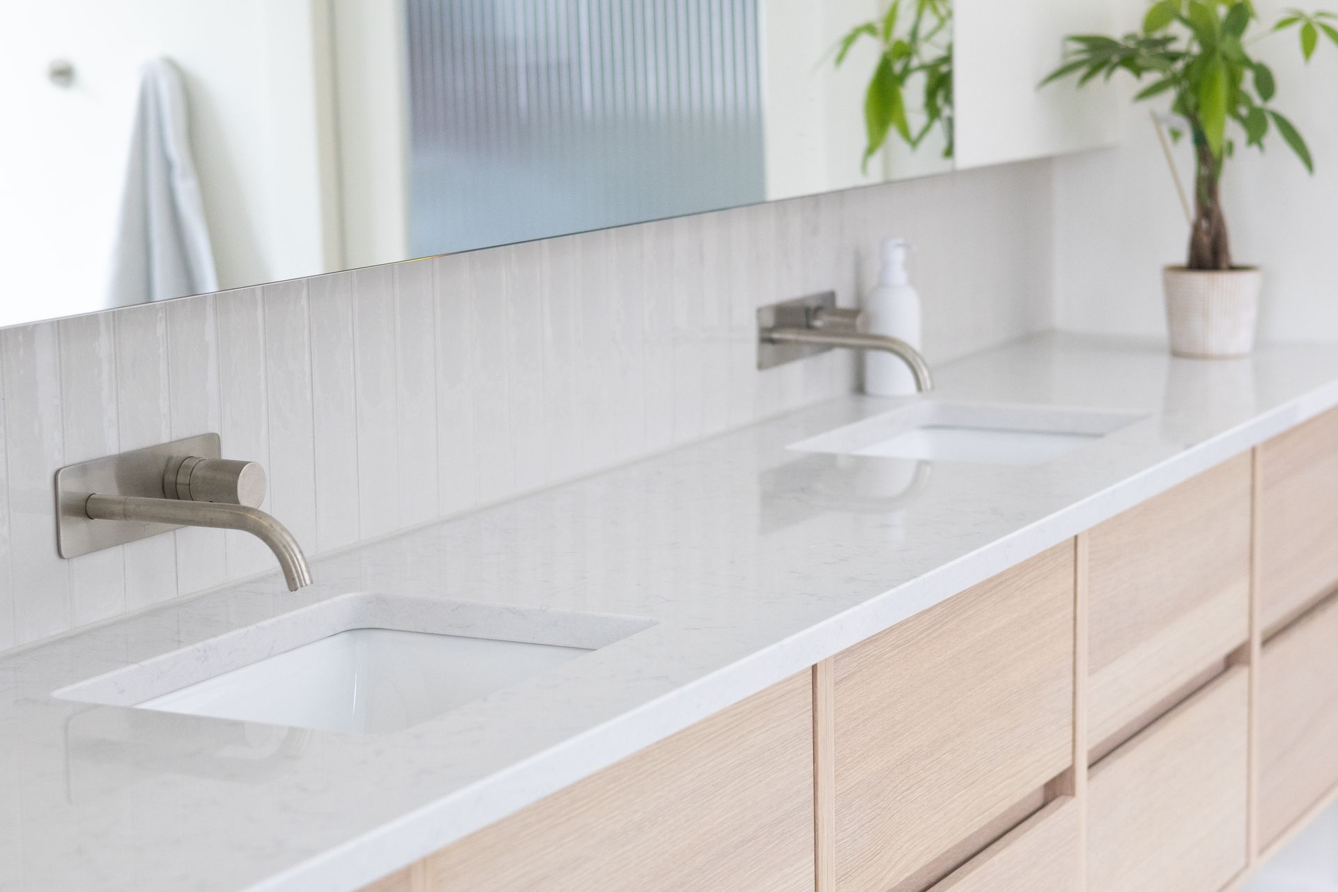 Salle de bain moderne avec comptoir blanc, deux lavabos et armoires en bois.