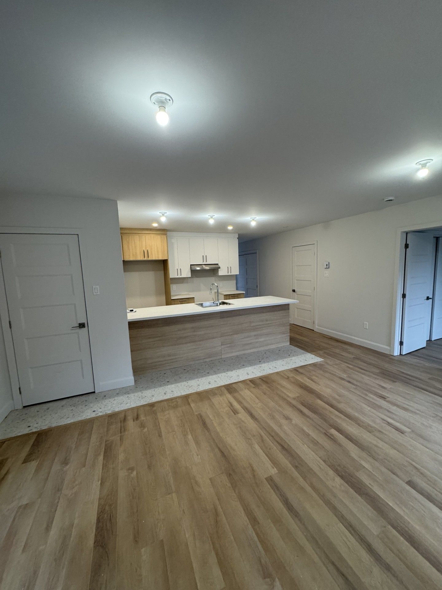 Cuisine et séjour à aire ouverte avec plancher de bois, armoires blanches et îlot en bois.