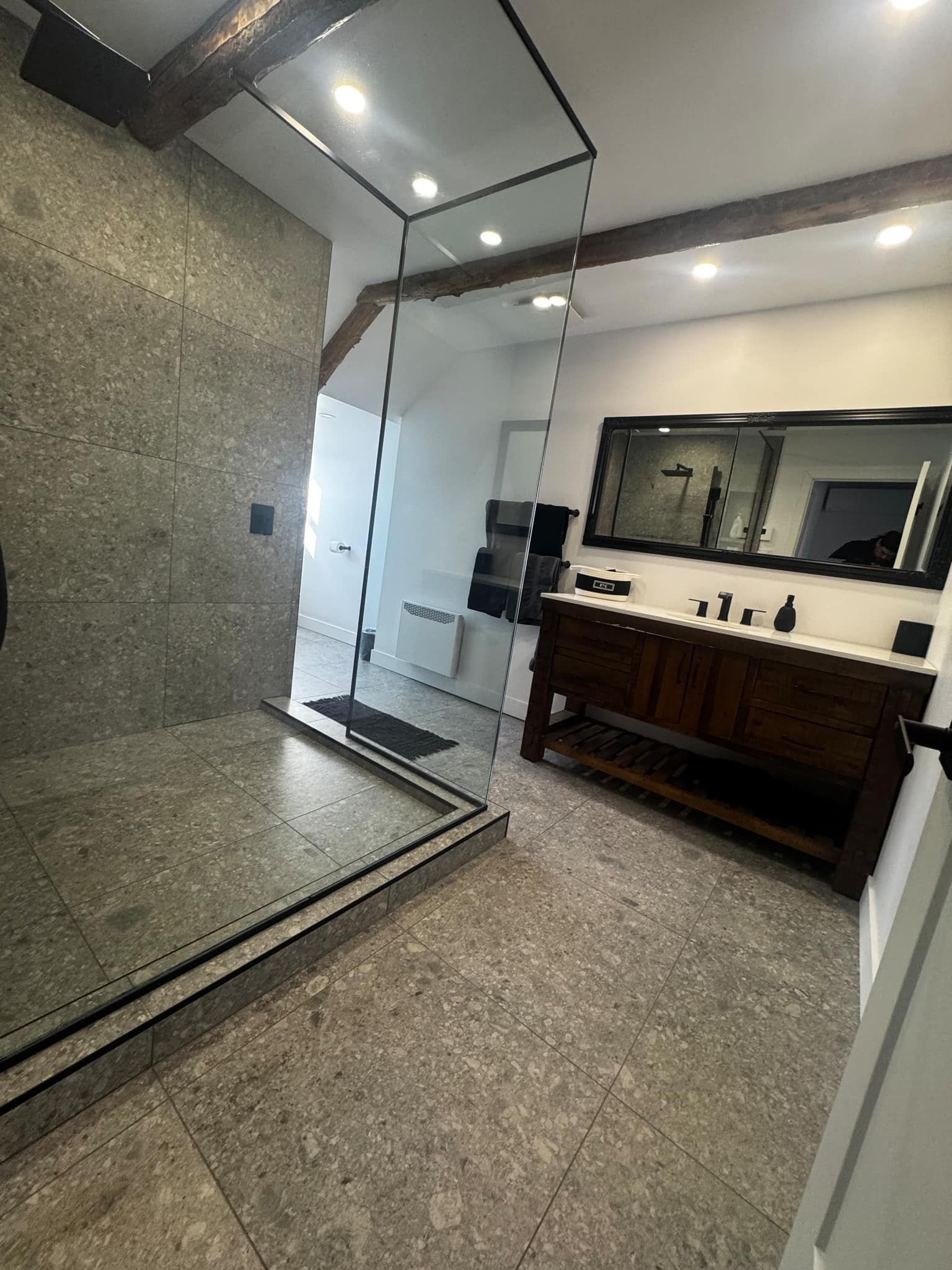 Salle de bains avec douche en pierre grise, parois en verre, meuble-lavabo en bois et grand miroir.