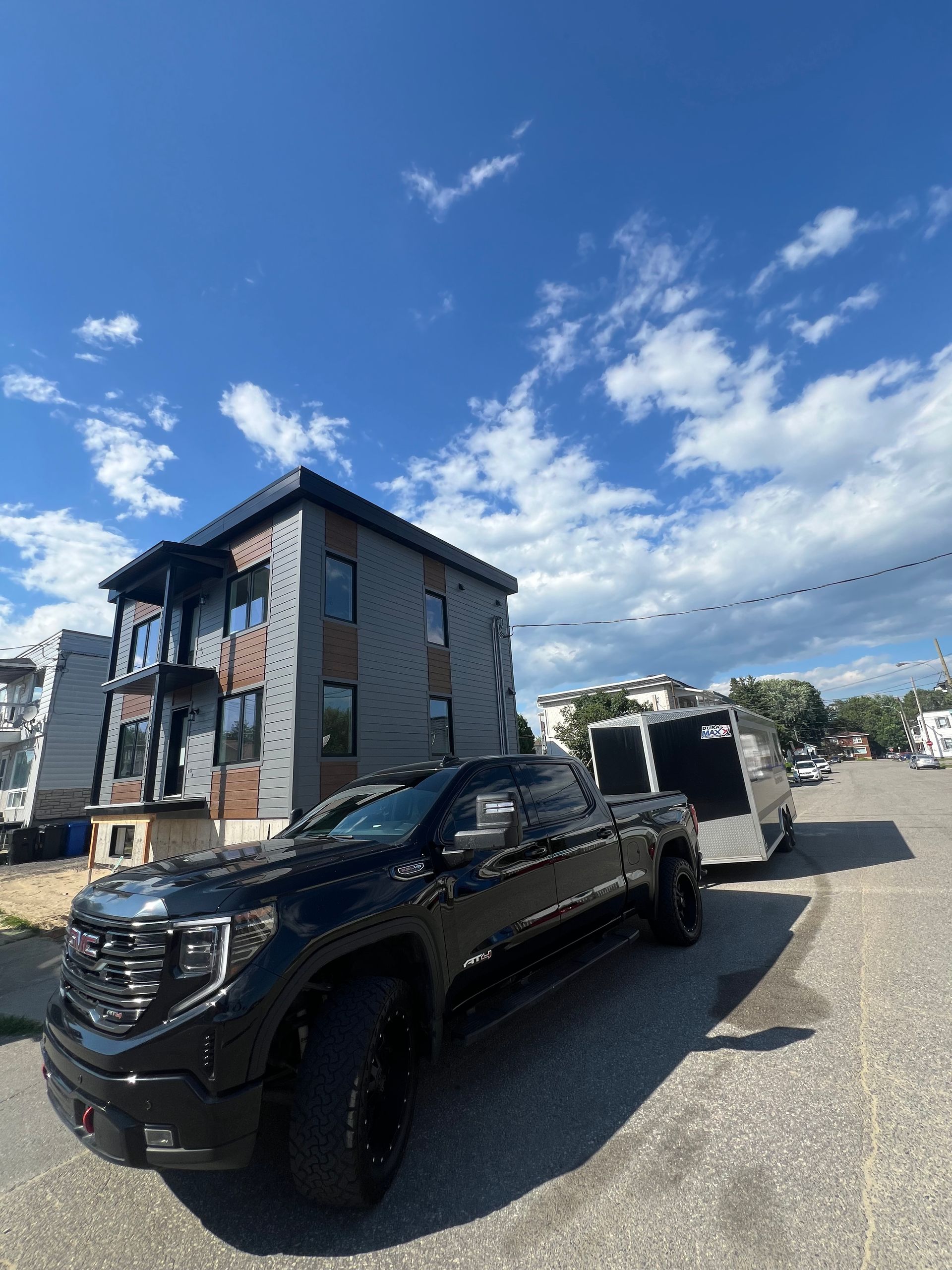 Un camion noir, avec une remorque attelée, est garé devant un bâtiment moderne, sous un ciel bleu partiellement nuageux.