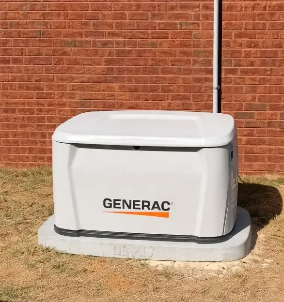 White Generac generator unit on a concrete pad beside a red brick wall.