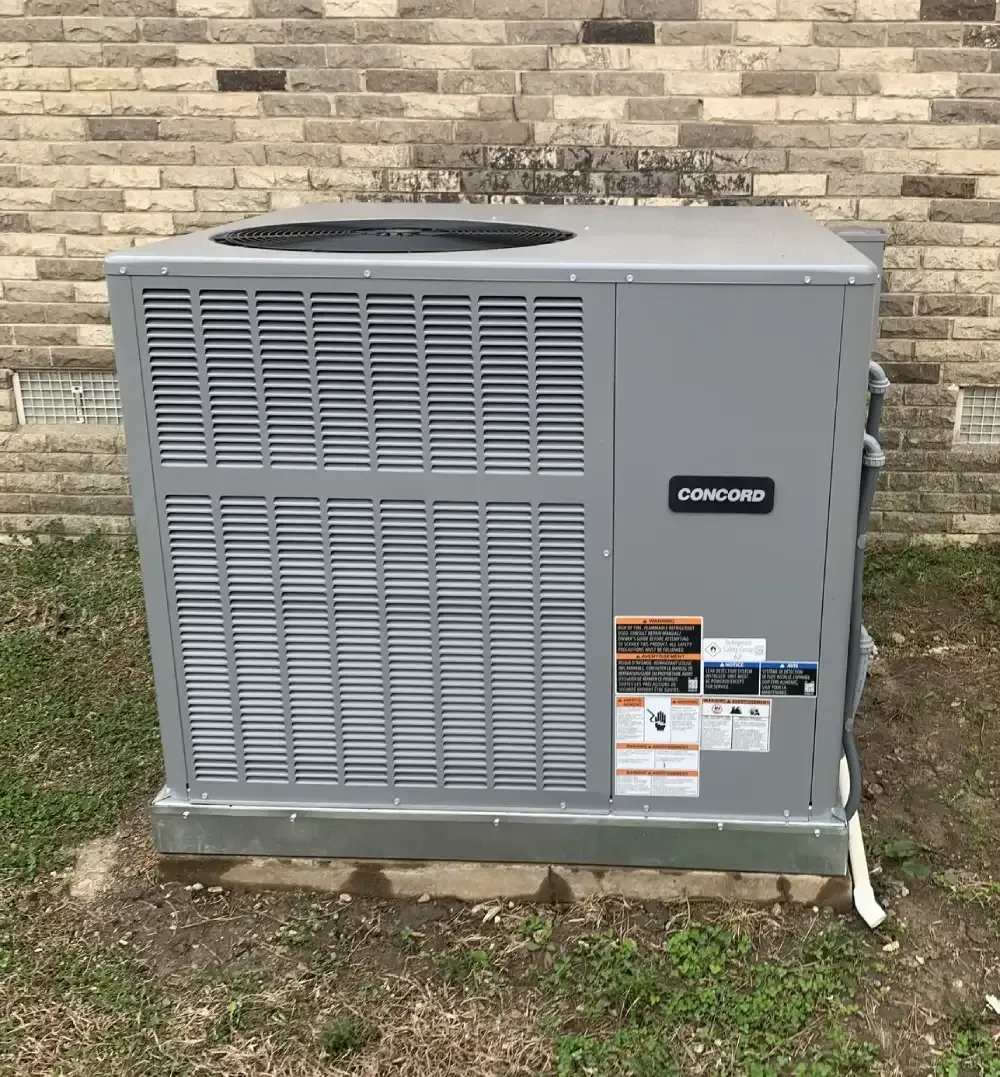 Gray outdoor HVAC unit beside a brick wall, with vented panels and a visible label.