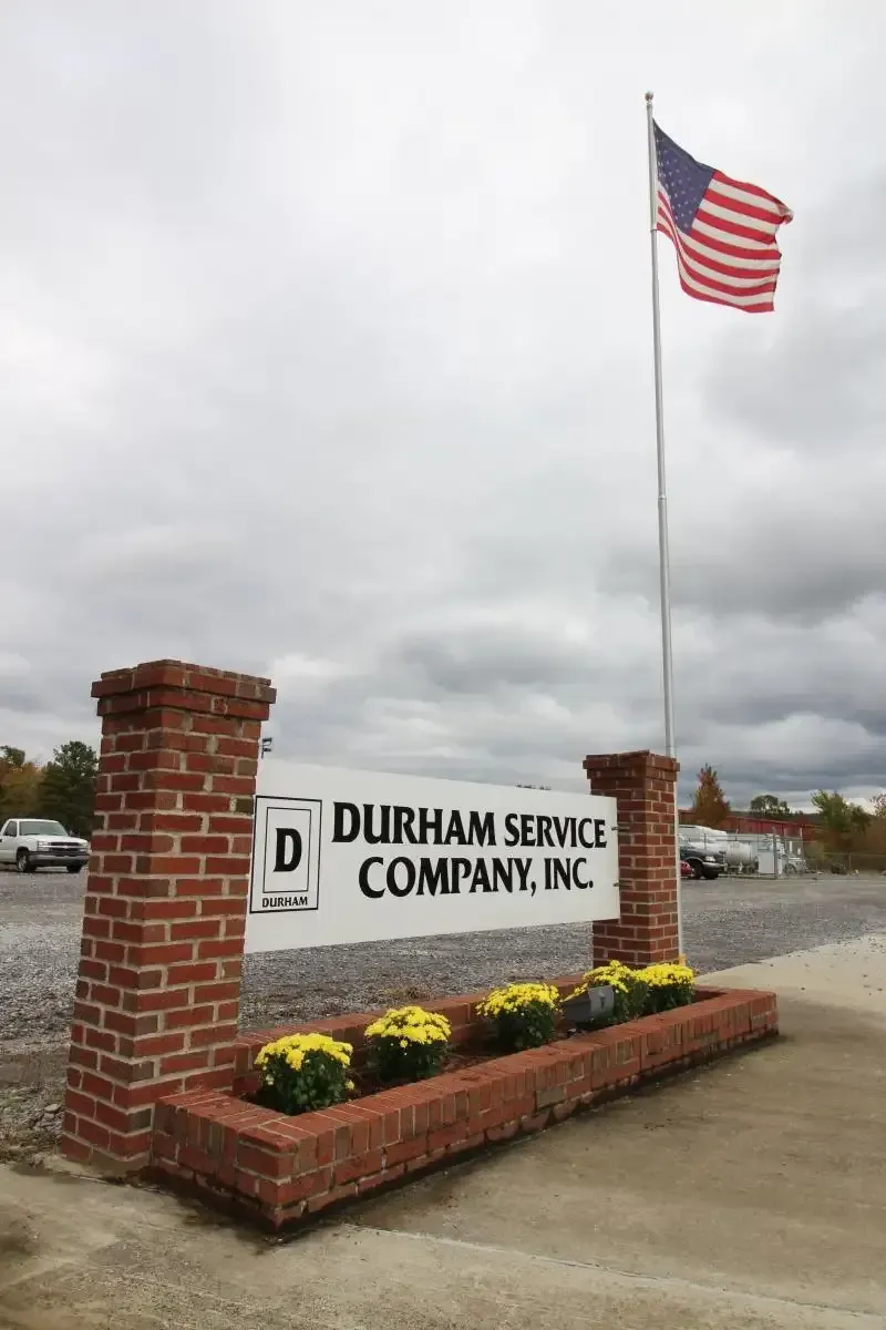 Durham Service Company sign with brick planter and U.S. flag outside under cloudy sky