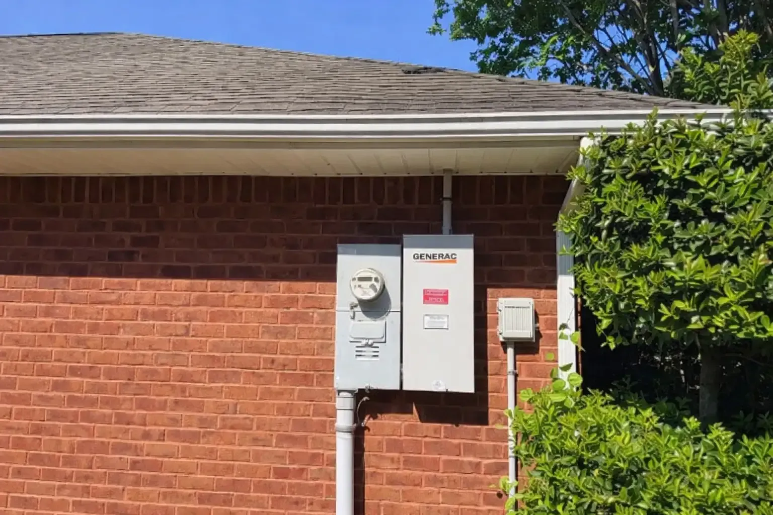 Brick house exterior with electric meter and utility box mounted on wall near roofline