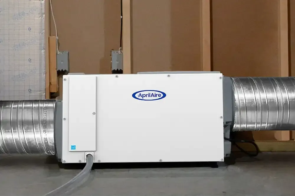 White HVAC ventilation unit connected to large metal ducts in a basement wall.