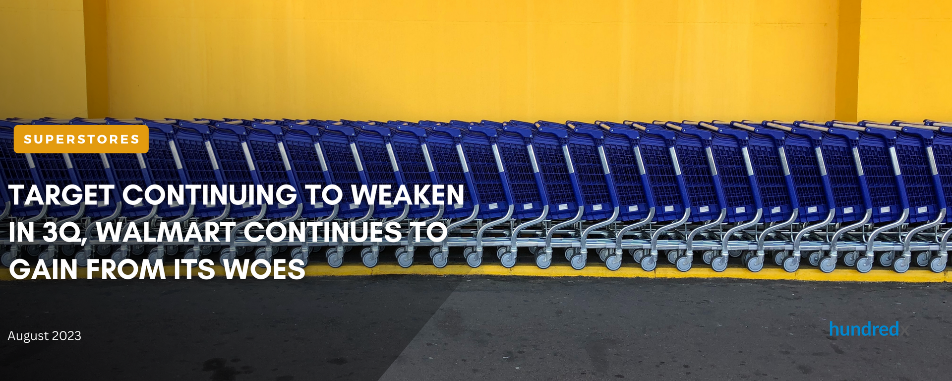 A row of blue shopping carts are lined up in front of a yellow wall.