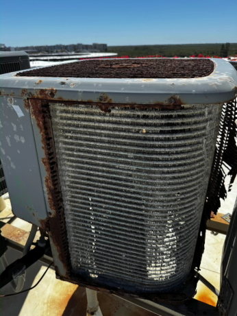 A rusty air conditioning unit on a rooftop, with a clear blue sky in the background.
