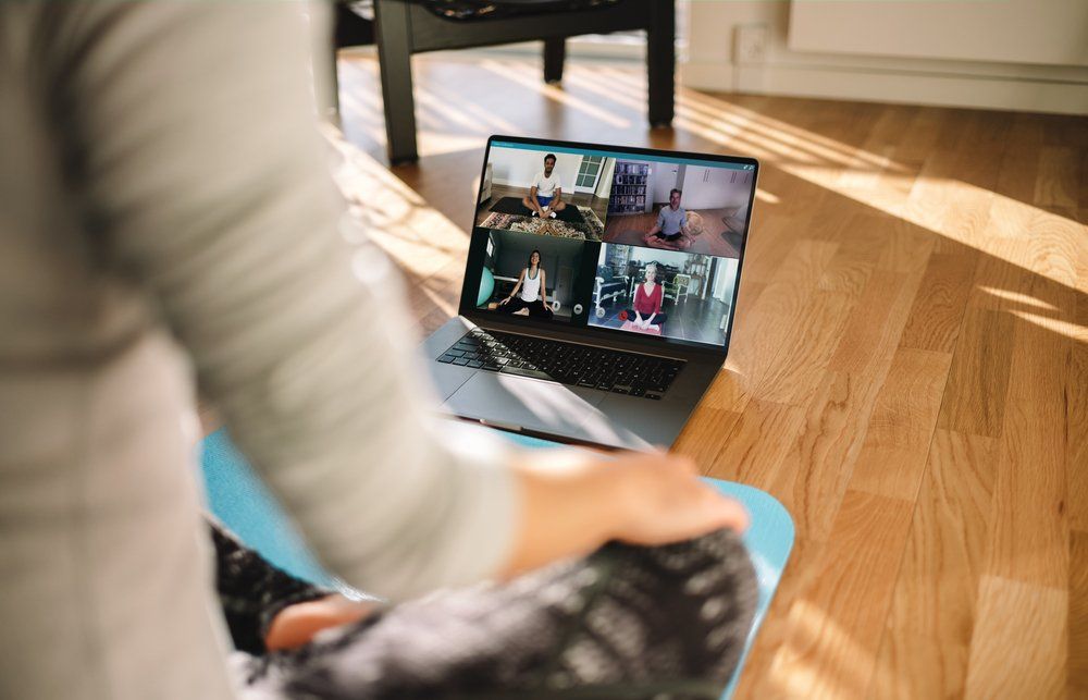 A person is sitting on a yoga mat in front of a laptop computer.
