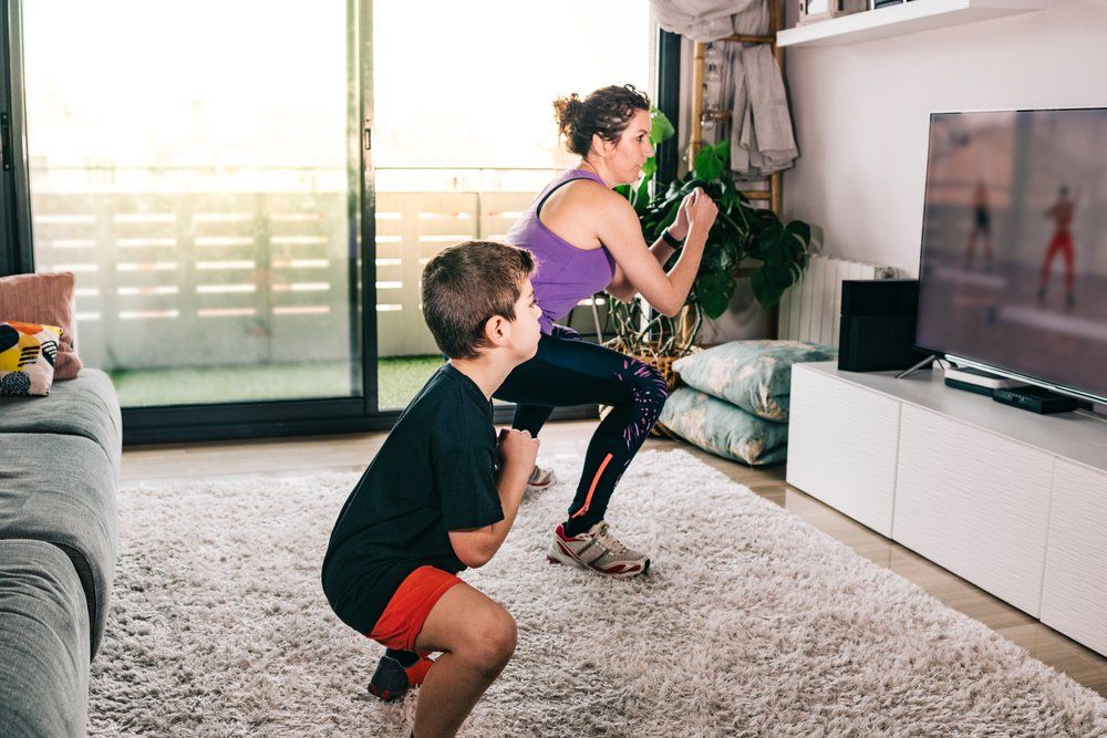 A woman and a boy are doing squats in a living room in front of a television.