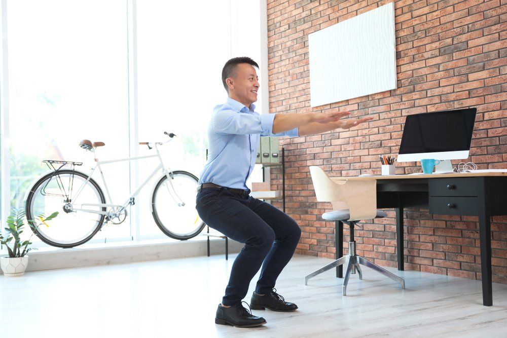 A man is squatting in an office in front of a computer.