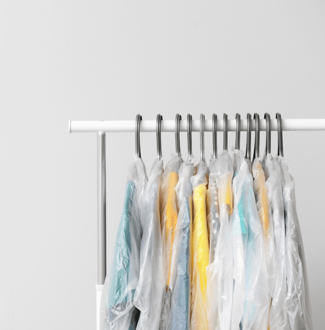 Clothes wrapped in plastic bags are hanging on a rack.