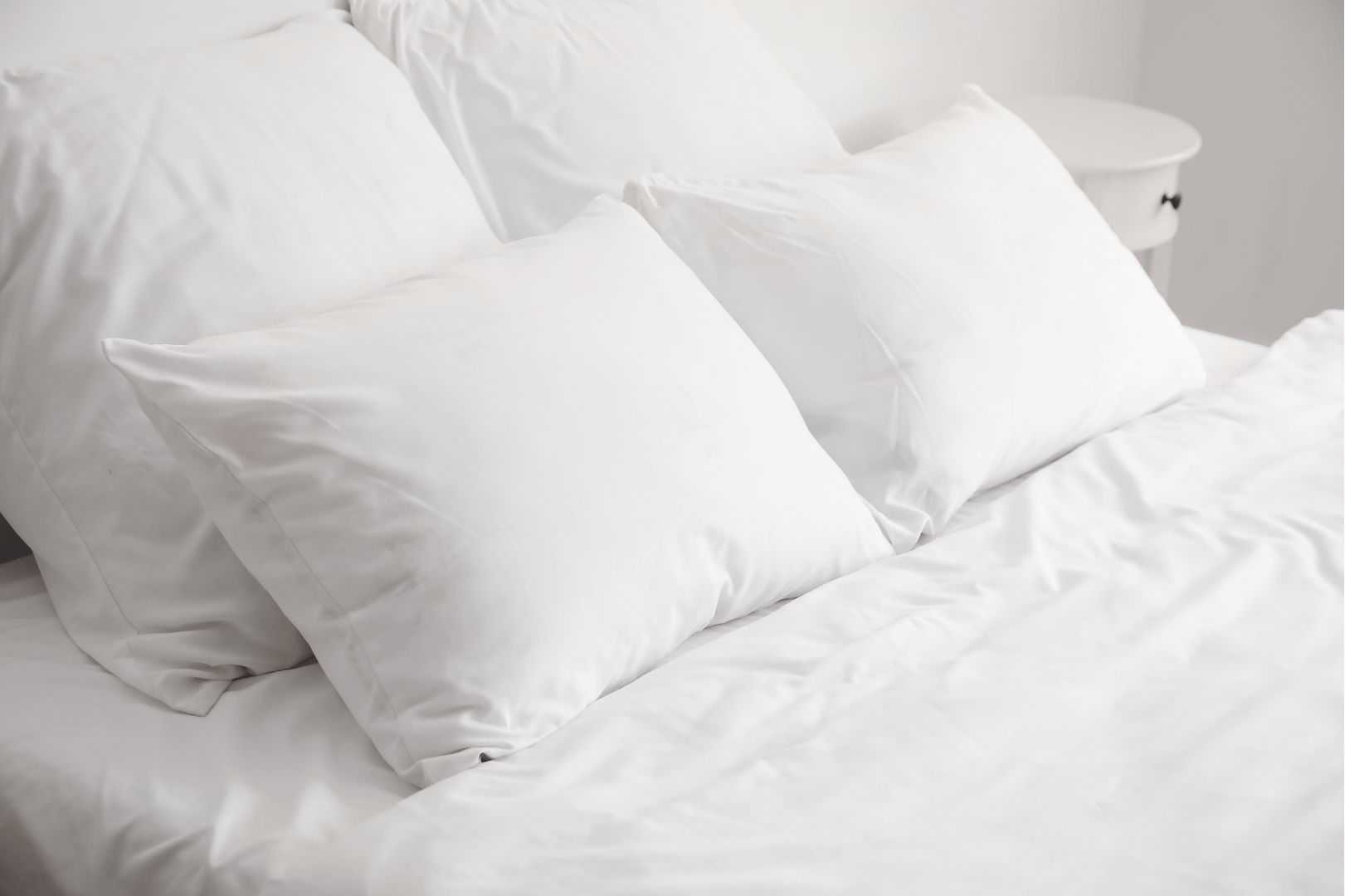 A bed with white sheets and pillows in a bedroom.