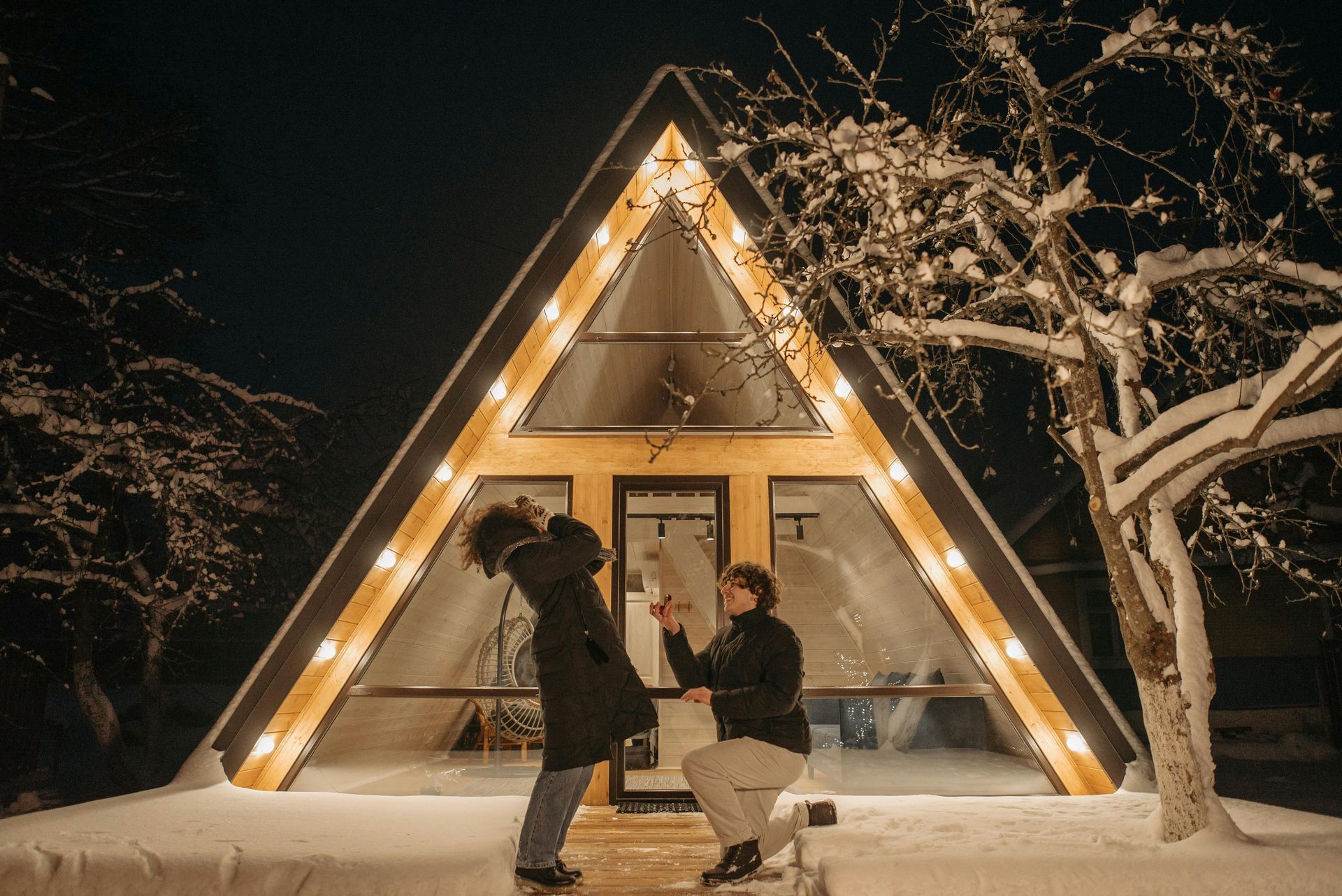 A man is proposing to a woman in front of an a frame cabin.