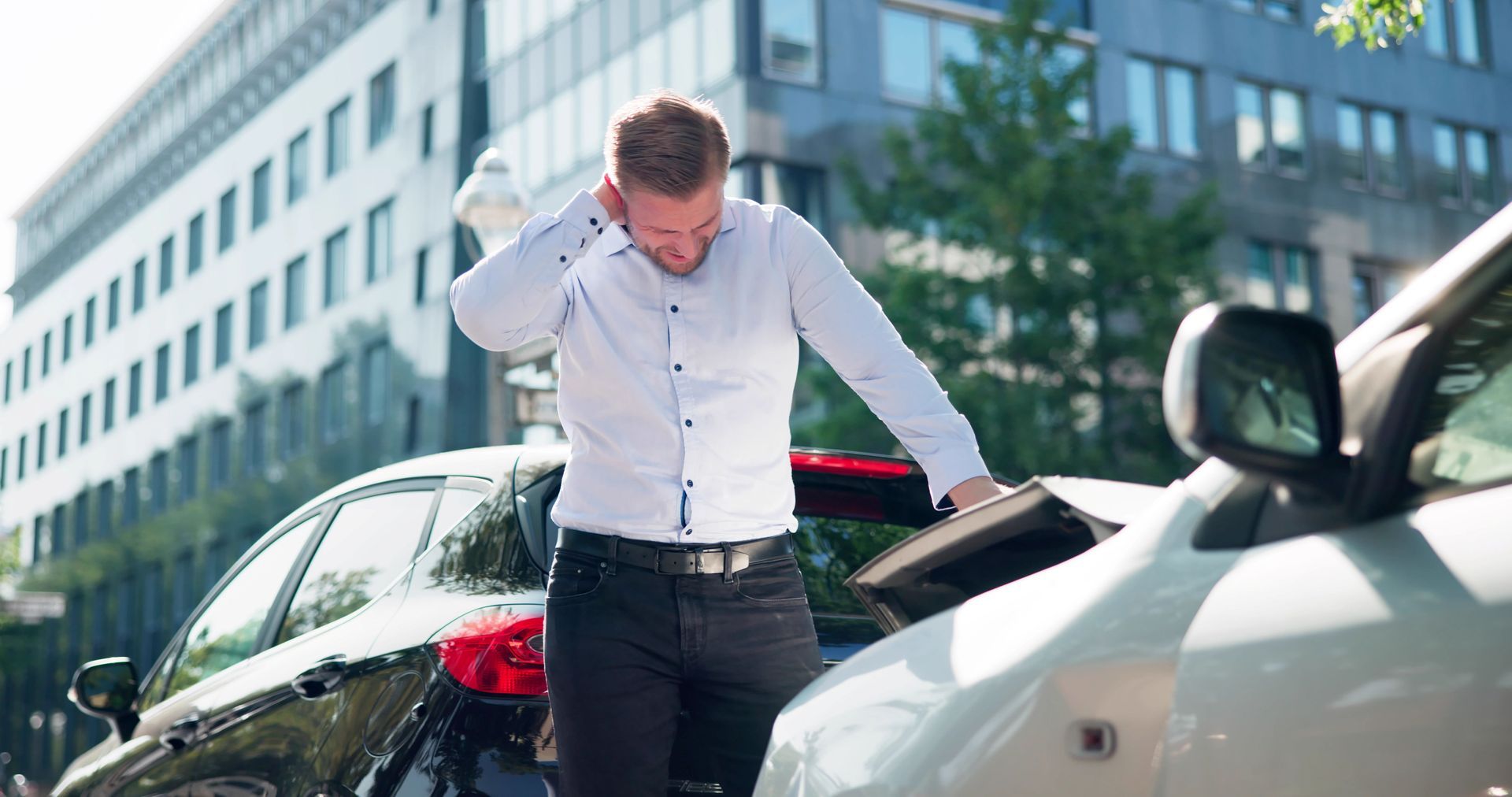 A driver is standing by two damaged cars, holding his neck after a collision A driver is standing by two damaged cars, holding his neck after a collision