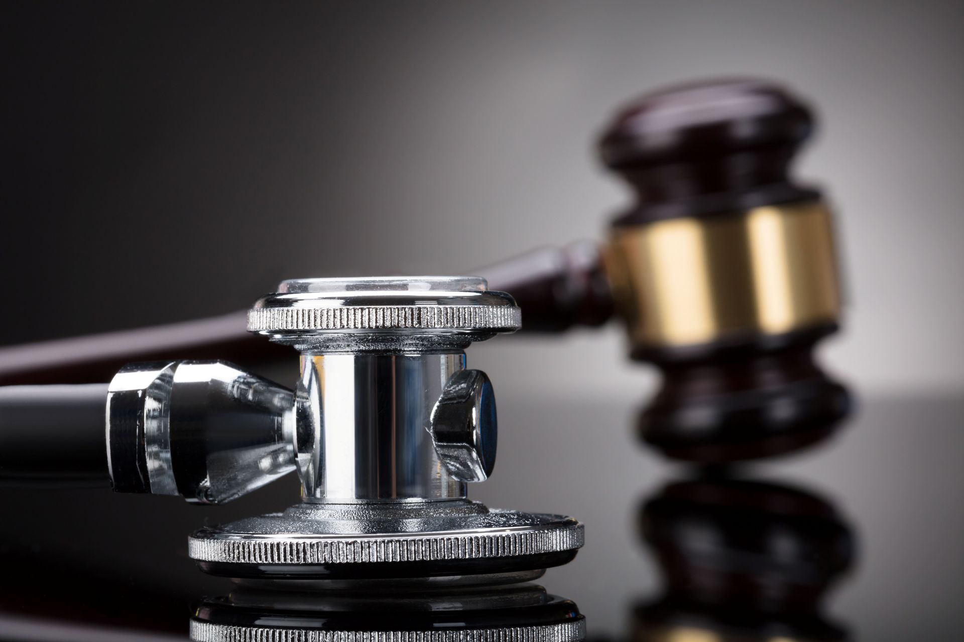 Close-up of a stethoscope on top of a black surface, with a blurry wooden gavel on the background.