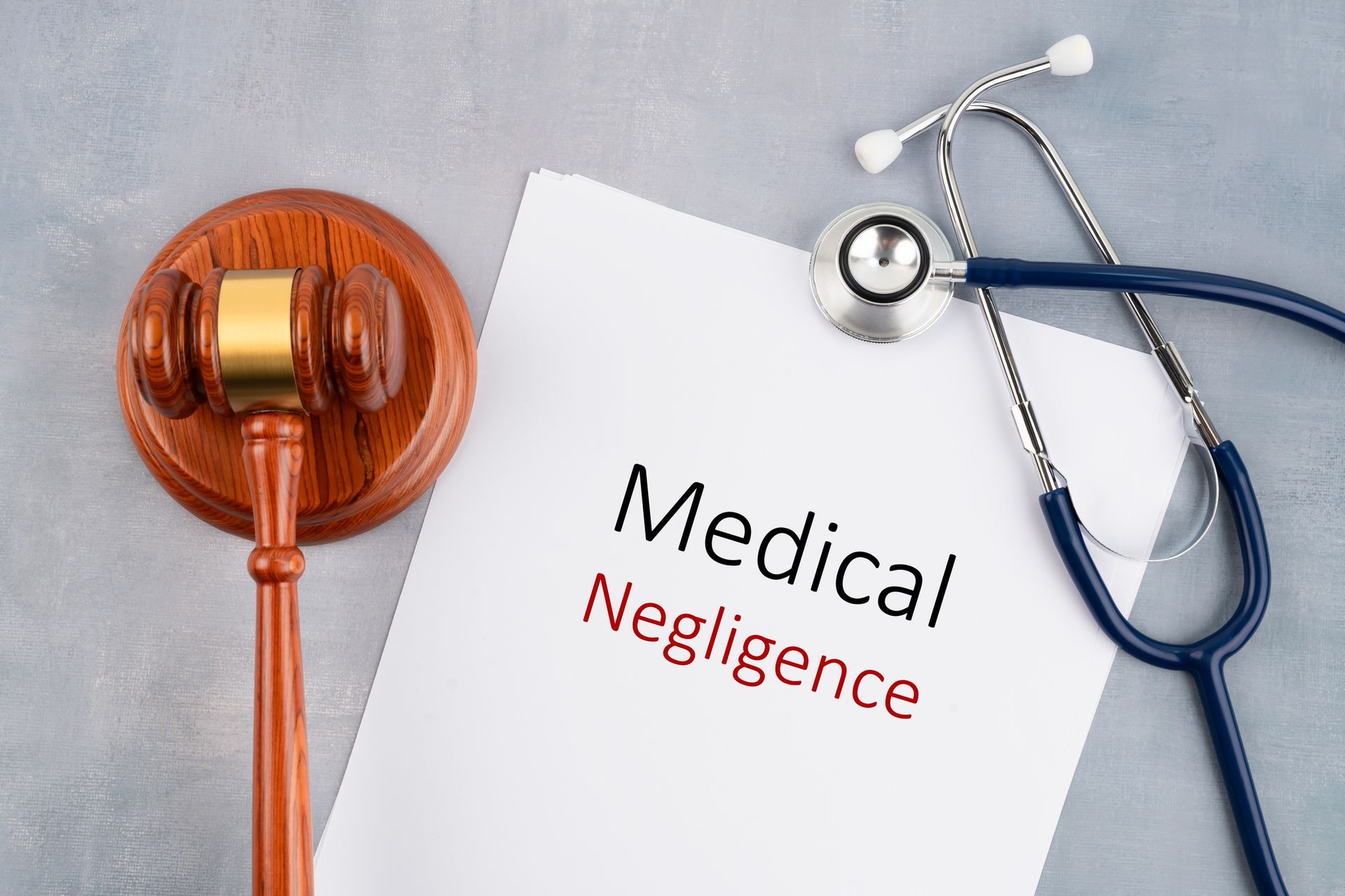 A gavel and stethoscope placed on a document labeled 'Medical Negligence' on a gray surface