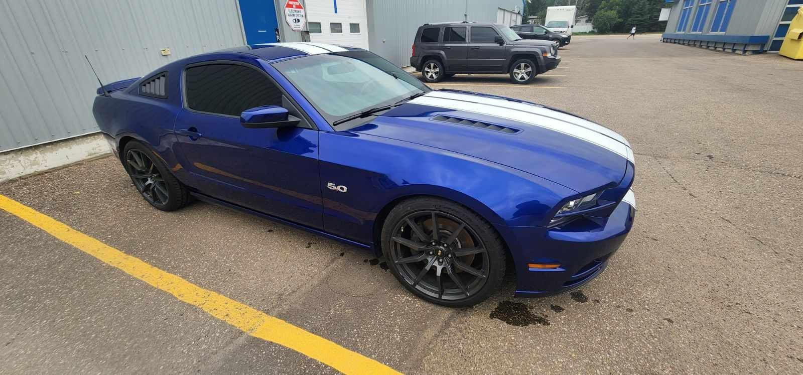 Blue Ford Mustang with white stripes parked on asphalt.
