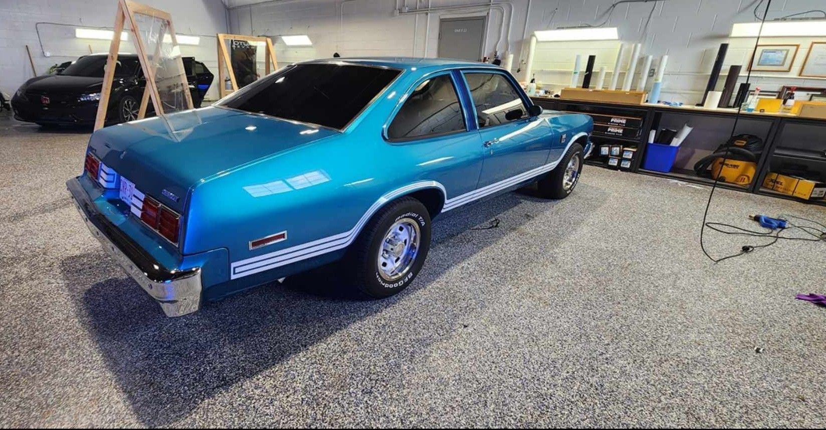 Blue classic car in a garage with tinted windows and white side stripes.