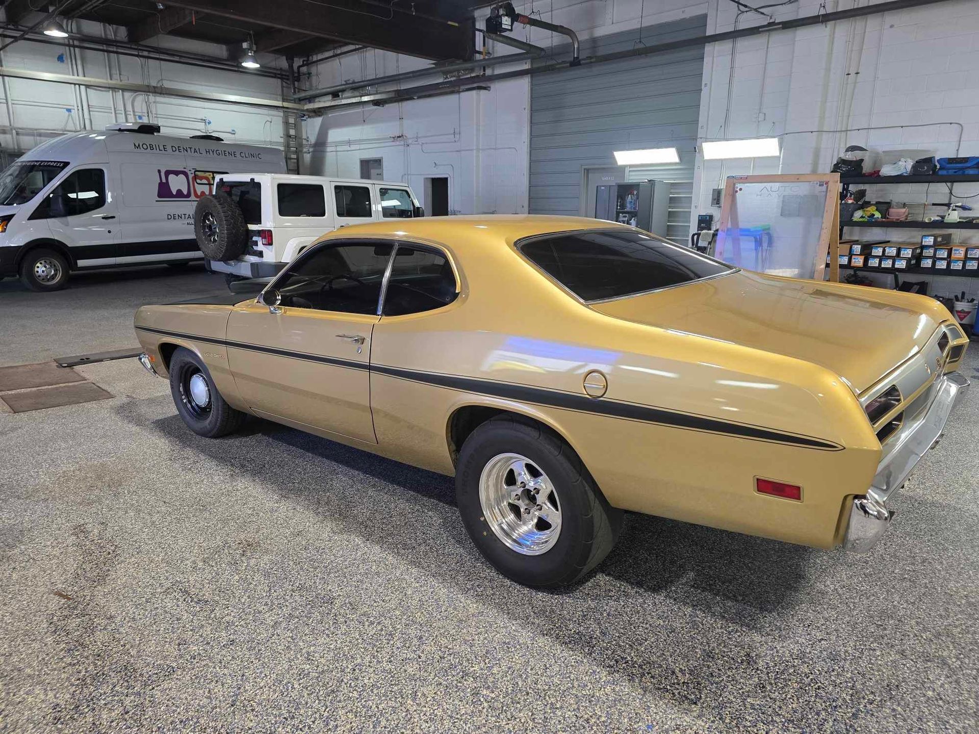 Gold classic car in a garage with a van and a white SUV.