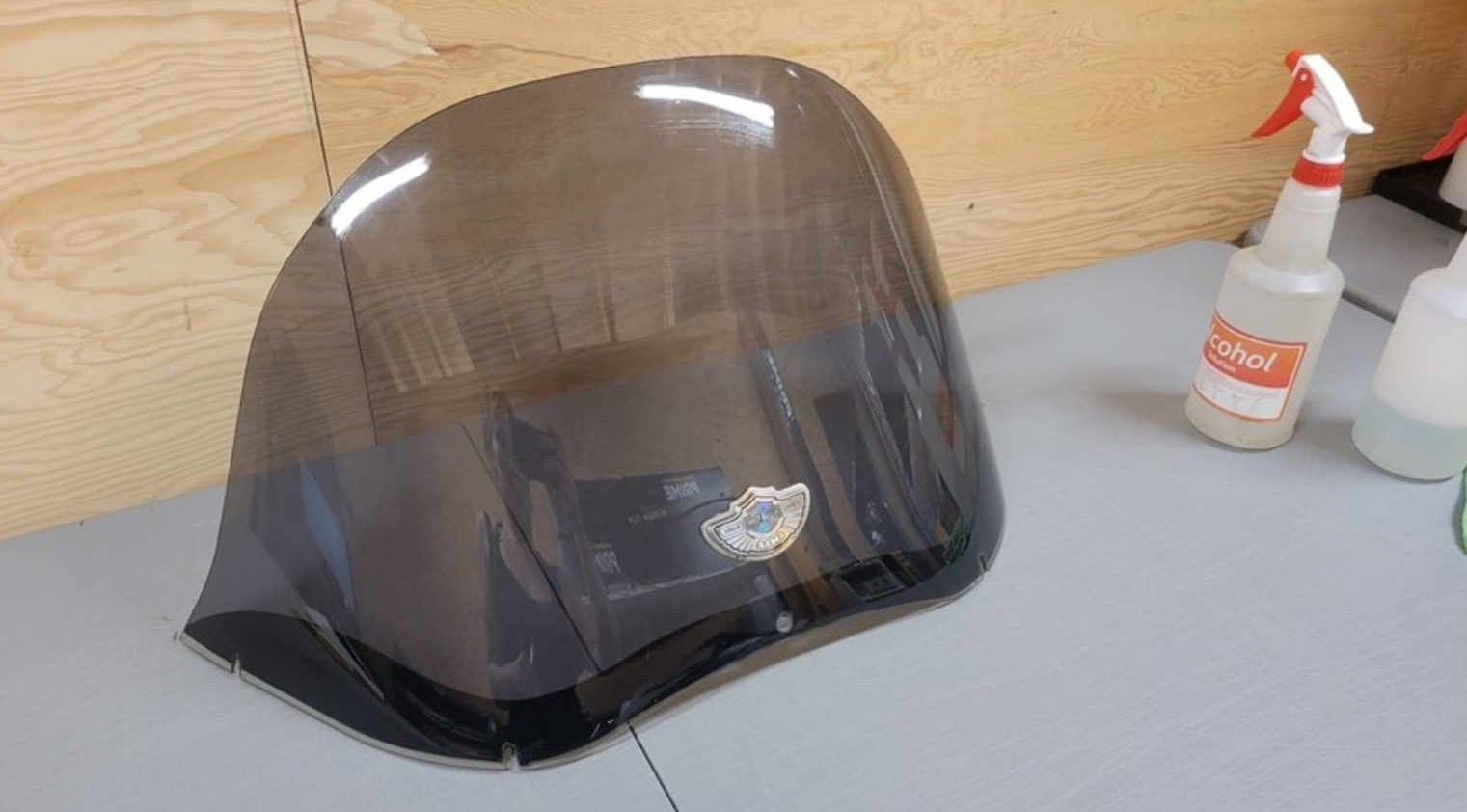 A dark, tinted motorcycle windshield sits on a gray surface with two spray bottles in the background.
