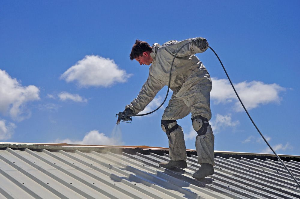 Man Using Airless Spray To Paint The Roof Of A Building — Enduro Shield Roofing Solutions in Elanora, QLD