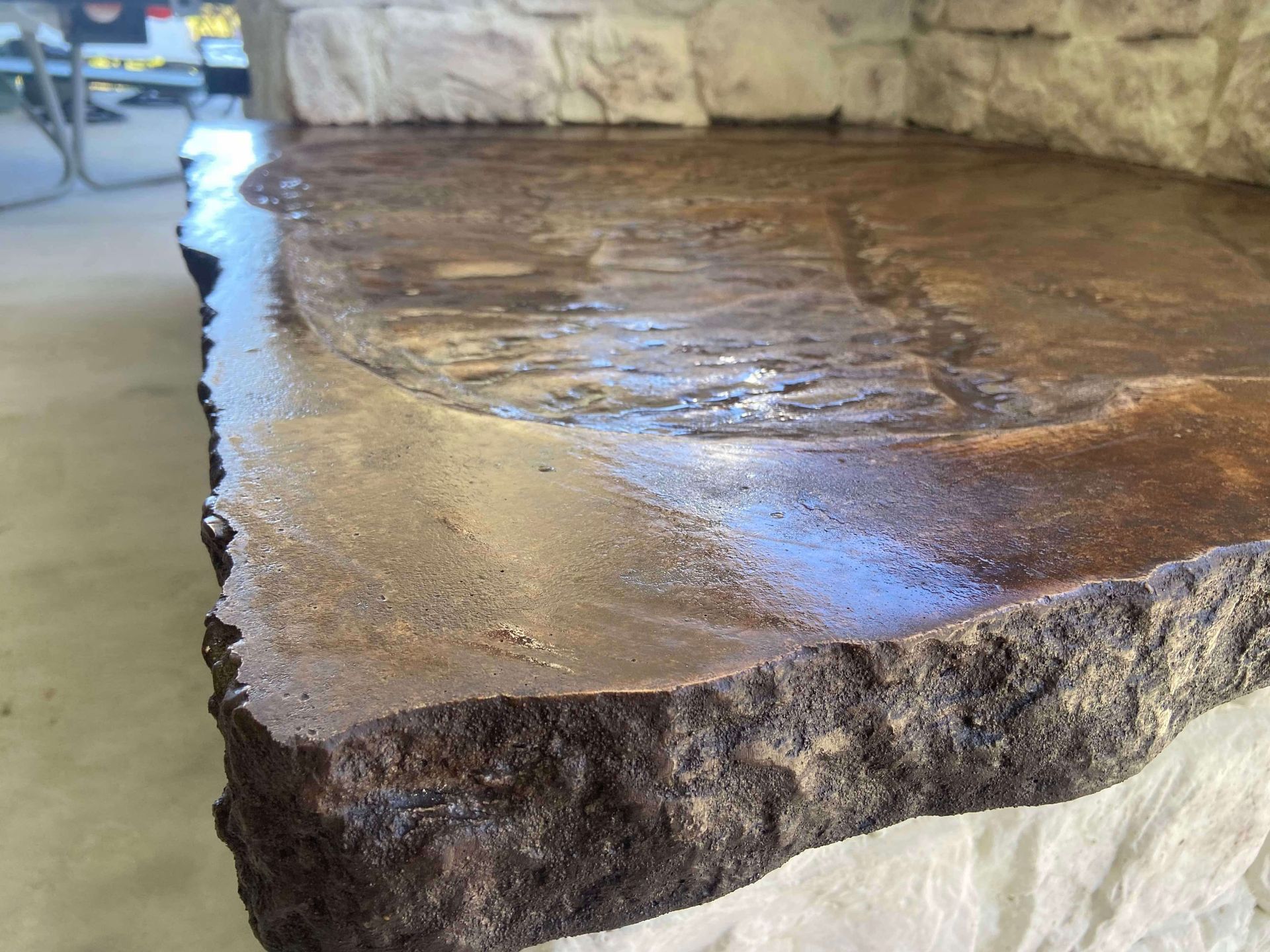 A large piece of stone is sitting on a concrete floor next to a stone wall.