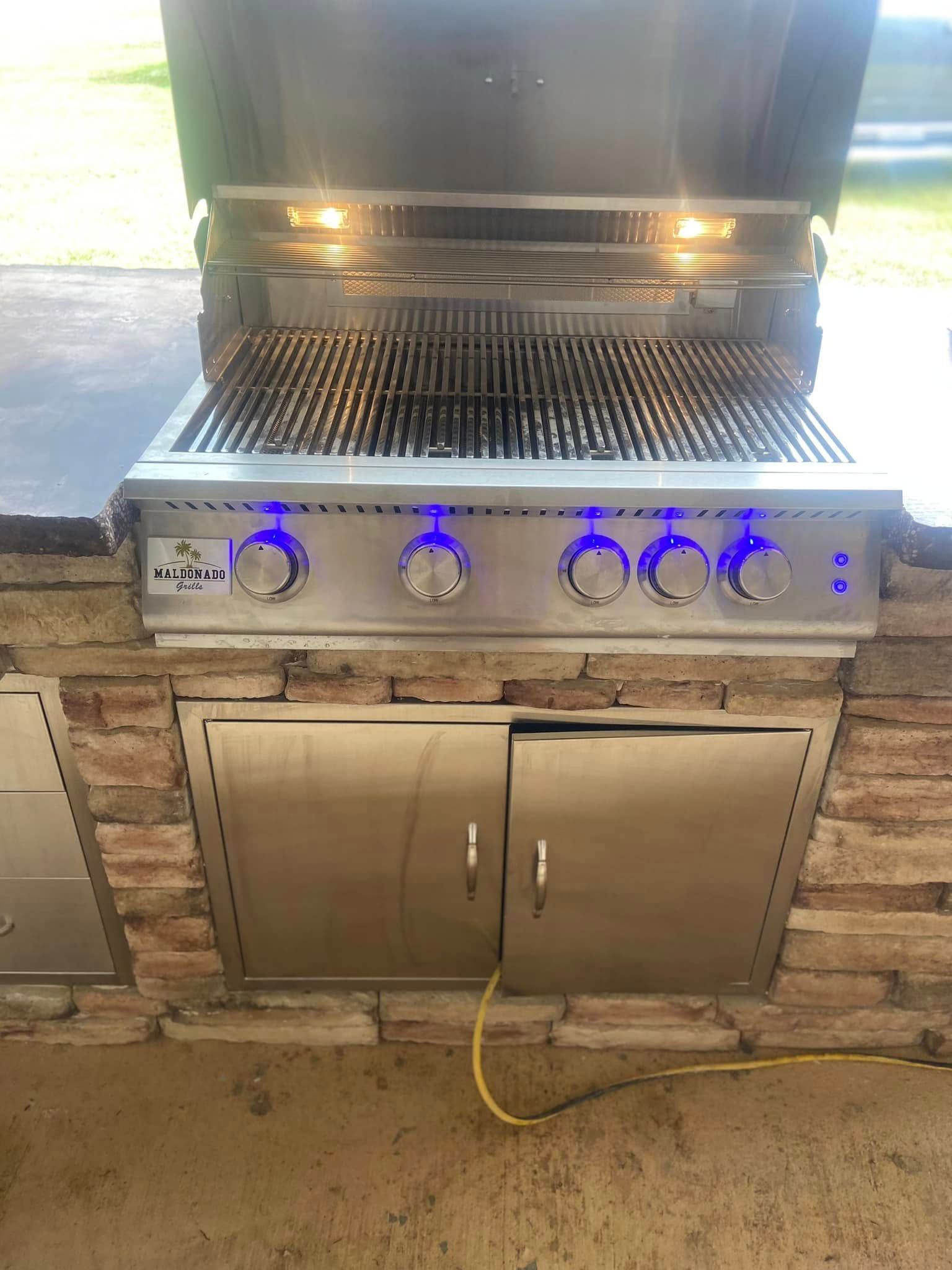 A stainless steel grill is built into a brick wall.