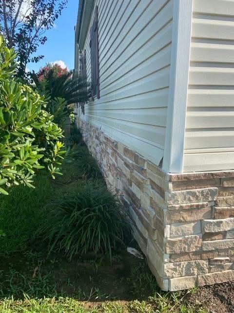 The side of a house with a stone foundation and siding.