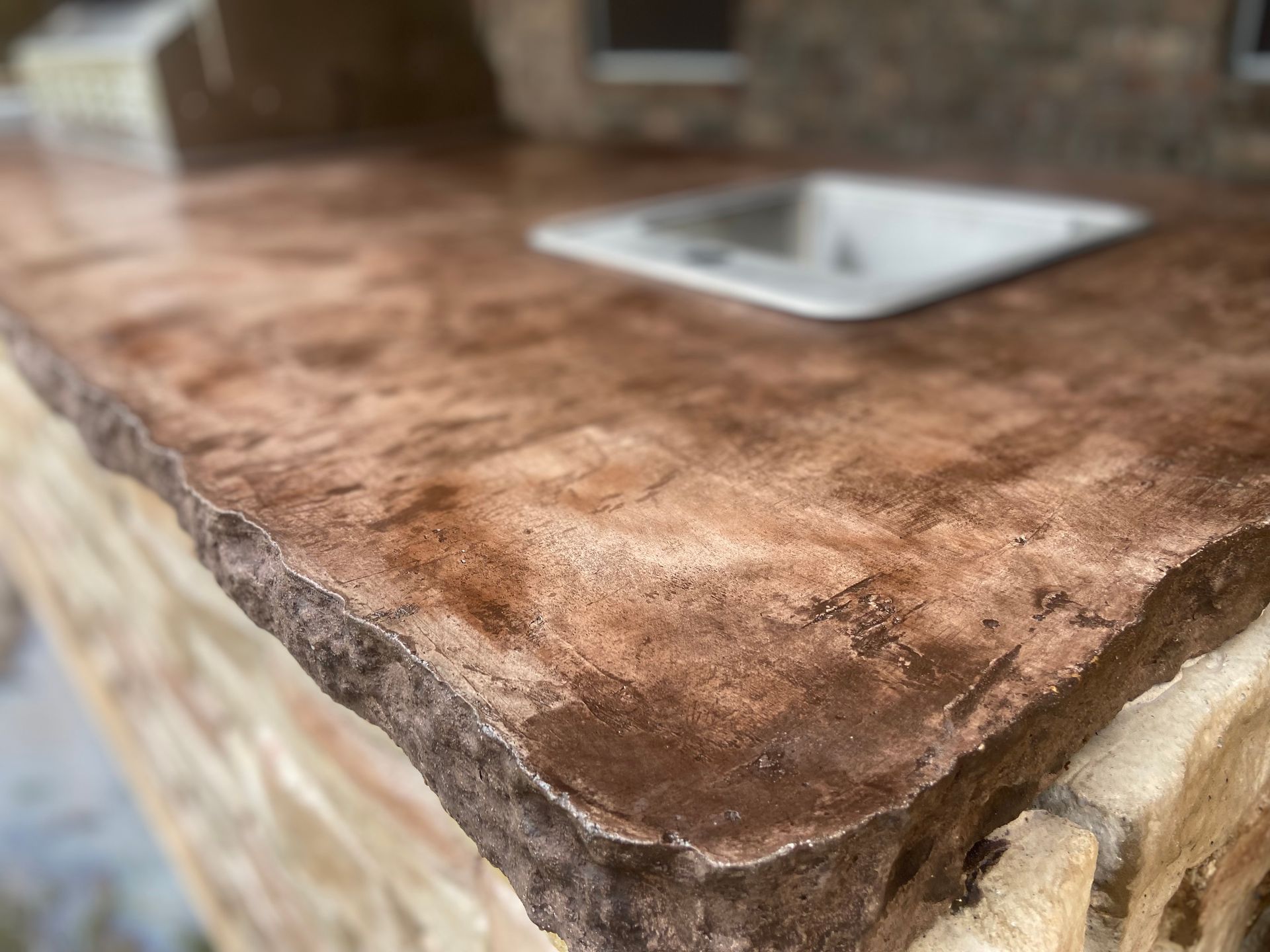 A close up of a concrete counter top with a sink in the background.