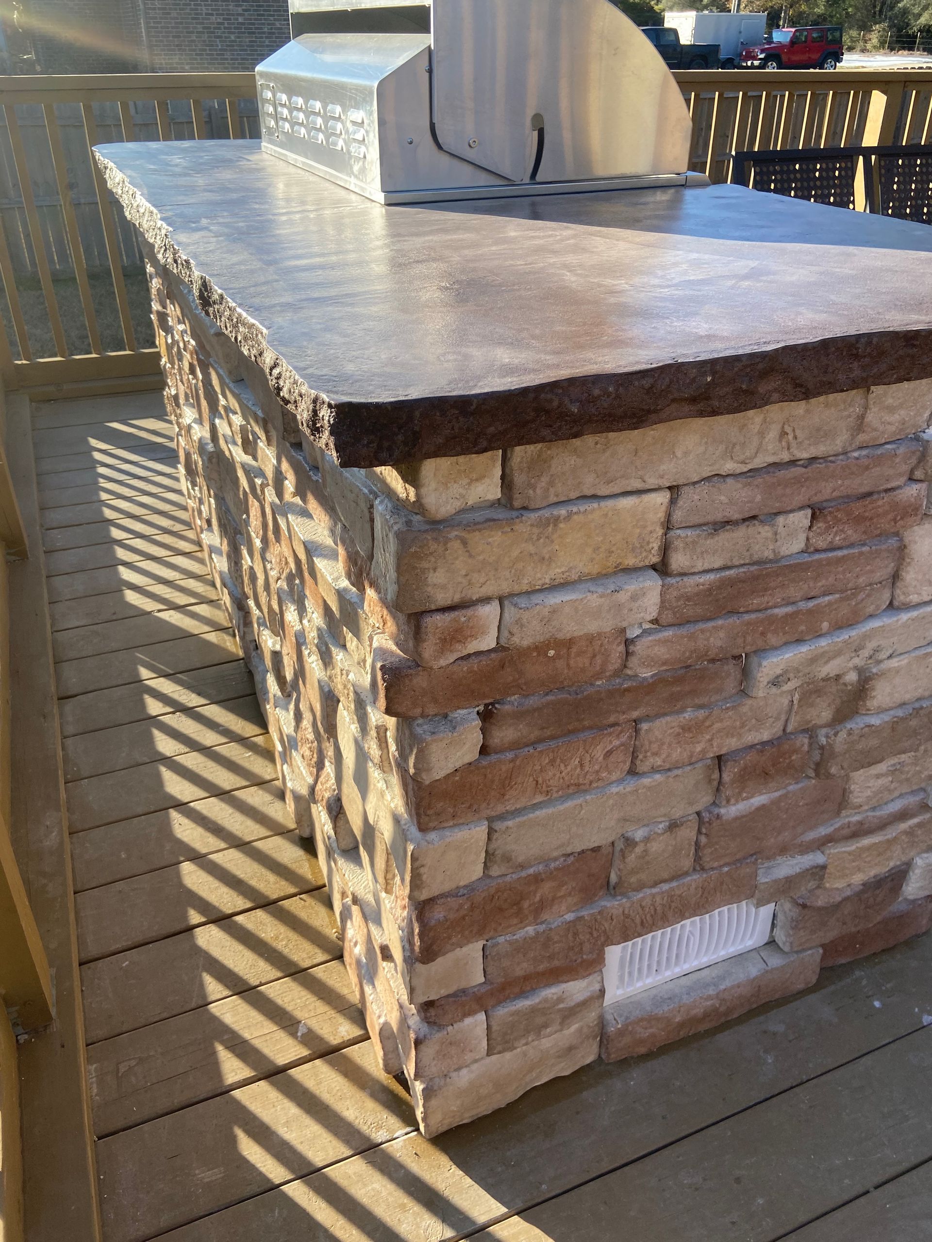A brick island with a grill on top of it on a deck.