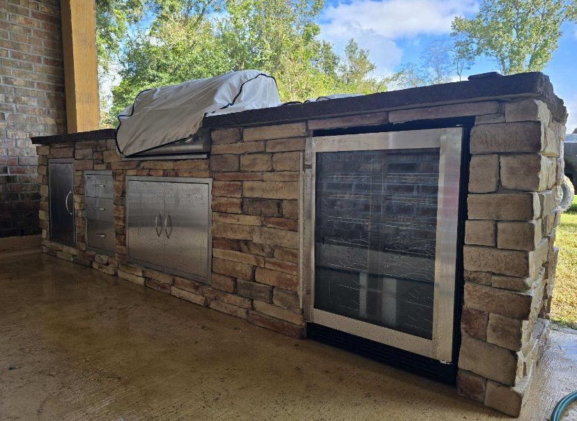 An outdoor kitchen with a grill and a refrigerator.