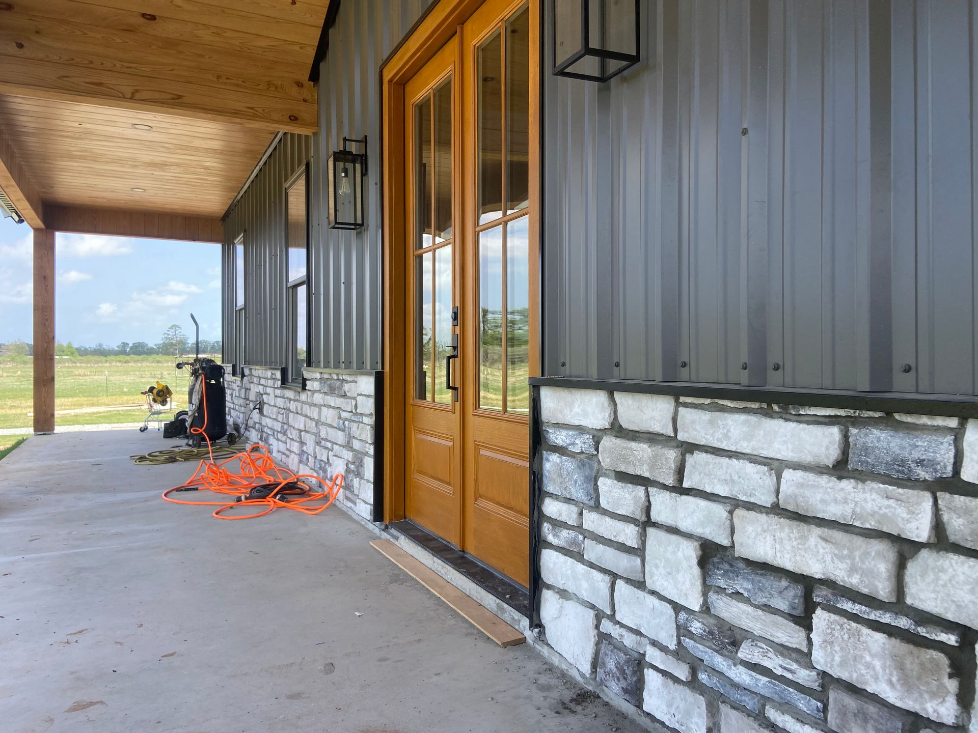 There is a porch with a wooden door and a brick wall.