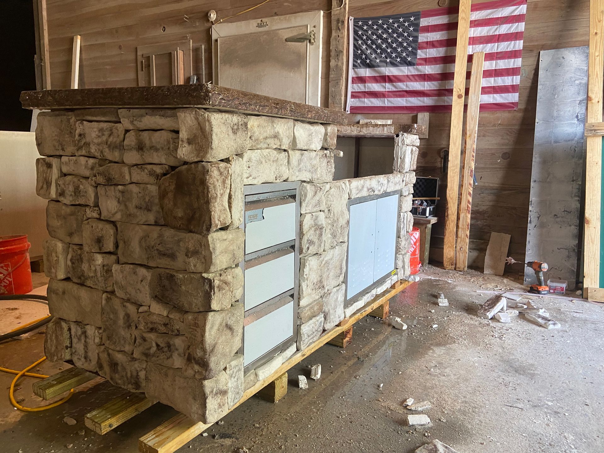 A stone bar is being built in a garage with an american flag in the background.