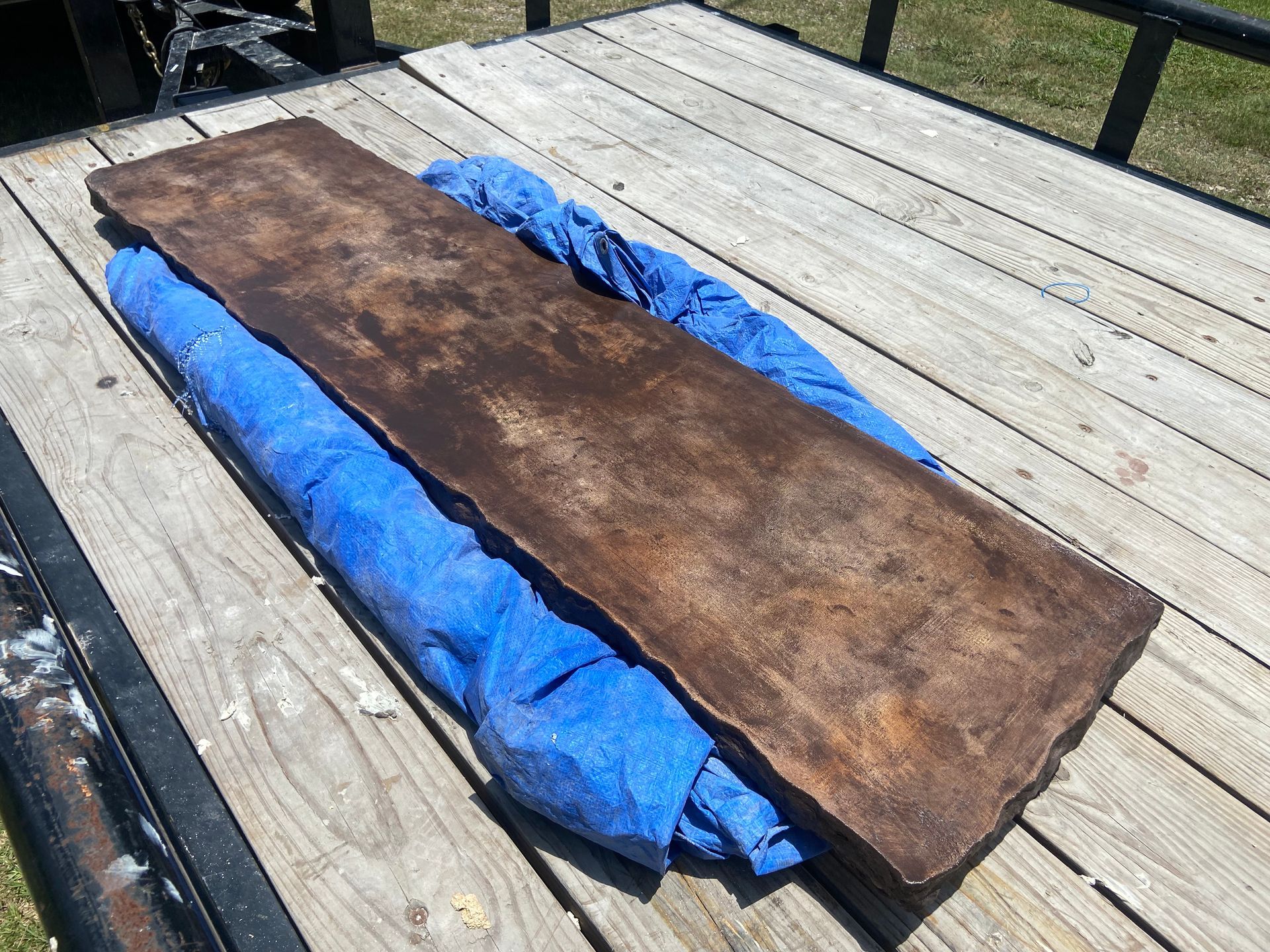 A piece of rusty metal is laying on top of a blue tarp on a wooden deck.